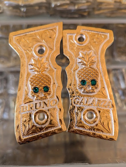 Custom engraved Colt 1911 pistol grips with pineapple design and green gemstone inlay.